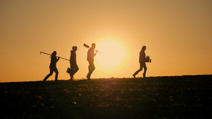 Amidst the fading light of the setting sun, a family of farmers is seen walking across a field,...