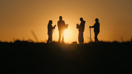 In the evening light, a group of farmers is seen chatting in a field at sunset, with their work...