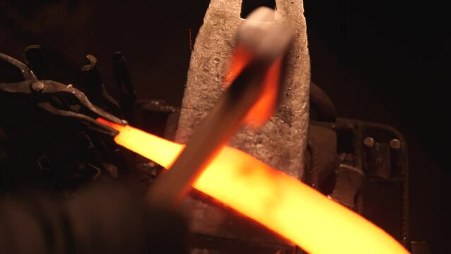 Close-up of blacksmith forging metal in workshop. man holds red-hot piece of steel with tongs and hits an anvil with hammer. shaping an iron product. blacksmithing production