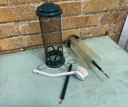 A bird feeder has been taken apart and cleaned and left to dry in sun. White Cleaning brush visible