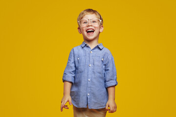 Cheerful funny little kid with blonde hair in eyeglasses, smiling brightly and looking at camera...