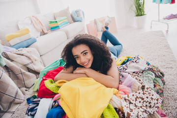 Full length portrait of nice young woman lying messy pile stack clothes flat indoors