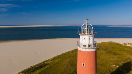 An aerial perspective of a majestic lighthouse standing tall on a sandy beach, its beacon shining...