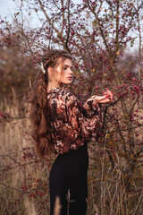Outdoor fashion portrait of young beautiful lady with braid hairstyle posing near hawthorn bush...