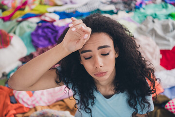 High angle view photo of young girl hand touch forehead pile stack clutter clothes apartment indoors