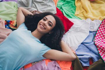 High angle view photo of young girl toothy smile lay pile stack clutter clothes apartment indoors
