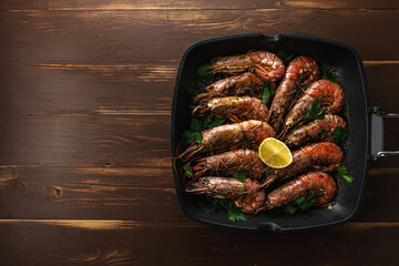 Fried shrimps on grill pan with fresh herbs and lemon slice. Seafood background. Top view.