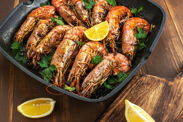 Fried shrimps on grill pan with fresh herbs and lemon slice. Seafood background.
