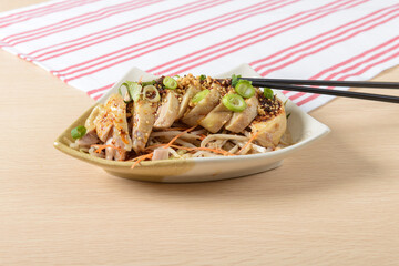 A delicious chicken salad with sliced meat, fresh garnishes, and seasoning served on a ceramic plate on a wooden table