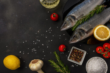 Two fresh seabass fishes with rosemary and vegetable on a black plate.