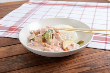 A white plate with Thai chicken curry and jasmine rice served on a wooden table with chopsticks resting on a checkered napkin