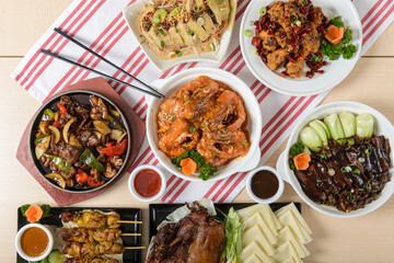 A variety of Asian cuisine spread out on a wooden table including meats, vegetables, and sauces for a savory meal