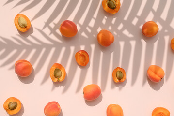 Apricot fruit with palm leaves shadow on a pastel pink background. Summer aesthetic concept.
