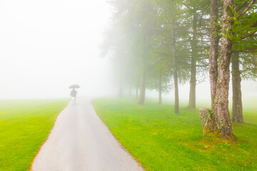 Man walking with an Umbrella on Golf Course with Fog in Crans Montana in Valais, Switzerland.