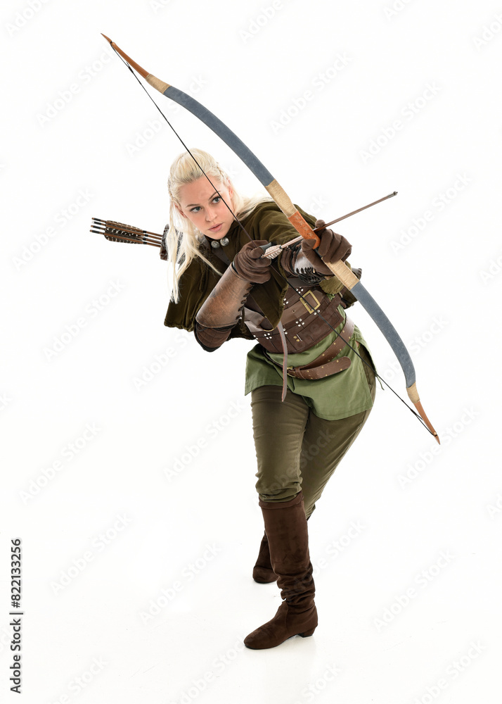 Poster full length portrait of blonde female model wearing green fantasy elf warrior halloween costume with leather armour. standing pose, holding weapons.  isolated on white studio background.