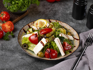 greek salad with green leaves, tomatoes, cucumber, feta cheese. dark grey background