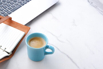 コーヒーを飲みながら、ノートパソコンとシステム手帳でデスクワークをしているイメージ
