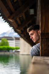 Fototapeta premium Side view of handsome young man leaning on bridge while thinking about life. Lucerne. Chapel bridge