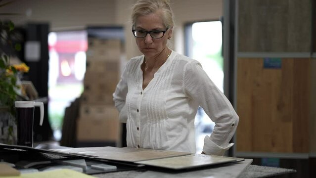 Mature woman thinking looking at samples of floor tiles in a store, consider using vct, lvp, or engineered tile in a home renovation redecorating project.