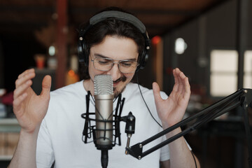 Man wearing glasses and headphones recording a podcast in a modern studio, speaking into a microphone. Concepts include media production, broadcasting, communication, and technology.