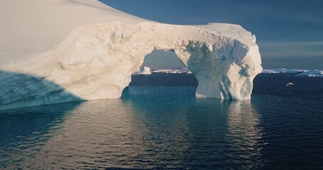 Melted ice cave arch hole iceberg towering arctic ocean. Big glacier floating cold water in sunset....