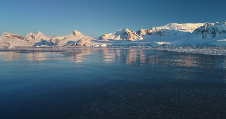 Explore icy wonders of Antarctica winter landscape. Snow covered mountain range in sunset light,...