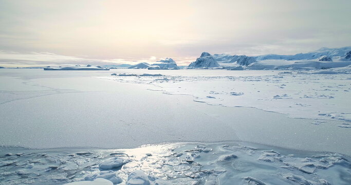 Fly over frozen Antarctic snow covered land in sunset. Untouched wilderness of South Pole. Desert white landscape, snow and ice aerial drone shot. Mountains in background. Nature polar conservation