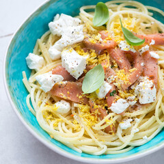 Close-up of lemony spaghetti served with smoked salmon and feta cheese in a turquoise bowl