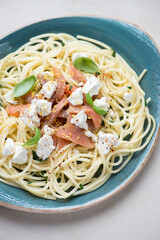 Plate of spaghetti with smoked salmon, feta cheese, lemon zest and green basil, vertical shot,...