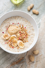 Bowl of peanut butter and banana oatmeal on a grey and roseate granite background, vertical shot
