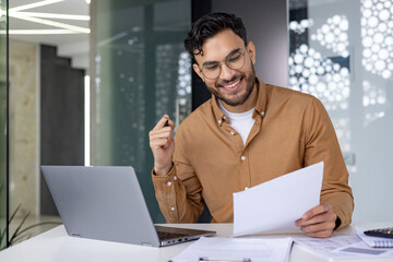 Businessman working on laptop and reviewing documents in modern office