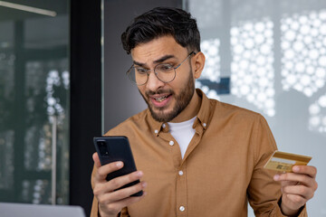 Man upset over online shopping issue while holding credit card and smartphone