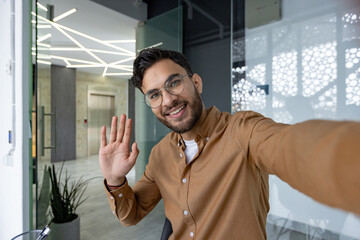 Smiling man waving in modern office during video call
