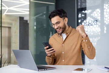 Excited man in office celebrating success while looking at his smartphone