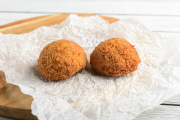 Two Falafel on a paper plate. The doughnuts are golden brown and appear to be freshly made. The paper plate is placed on a wooden cutting board