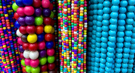 Colorful glass and natural stone beads hanging in a row as a background. Multicolored handicraft...
