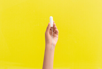 The girl is holding tampon in her hand. Yellow background. Period. Feminine hygiene products. Top view. Space for text.