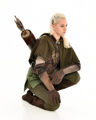 full length portrait of blonde female model wearing green fantasy elf warrior halloween costume with leather armour. sitting pose kneeling. isolated on white studio background.