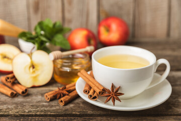 Fragrant hot tea with cinnamon stick and anise on a textured wooden background. A cup of hot tea with honey, lemon, mint and apples. Spicy tea with spices. Immunity tea. Health concept.Copy space.