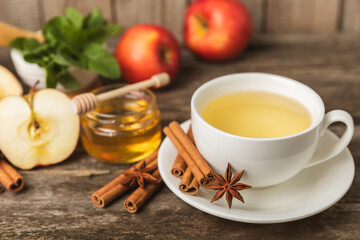 Fragrant hot tea with cinnamon stick and anise on a textured wooden background. A cup of hot tea with honey, lemon, mint and apples. Spicy tea with spices. Immunity tea. Health concept.Copy space.
