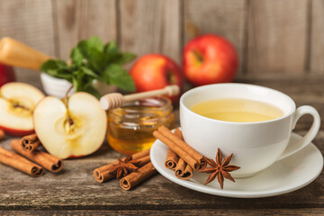 Fragrant hot tea with cinnamon stick and anise on a textured wooden background. A cup of hot tea with honey, lemon, mint and apples. Spicy tea with spices. Immunity tea. Health concept.Copy space.