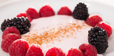 Raspberries and blackberries laid out on a white plate in circle with yogurt and cinnamon