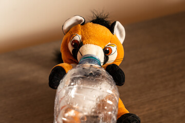 cute puppet representing a raccoon drinks from a plastic bottle, holding the bottle with his paws 