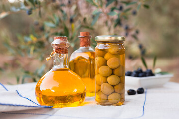 still life of olives and oil on a table against a background of olive trees