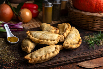 Homemade meat, chicken, ham and cheese empanadas on wooden board and vegetables around and...