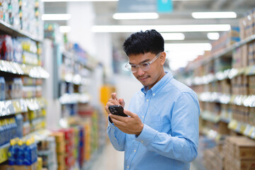 A man is looking at his cell phone in a store. He is wearing glasses and a blue shirt