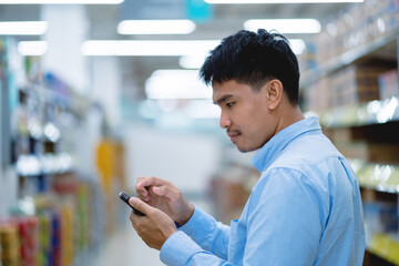 A man is looking at his cell phone in a store. He is wearing glasses and a blue shirt