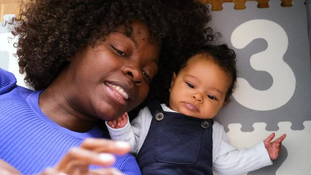 African woman is laying on the floor with a baby reading a book.