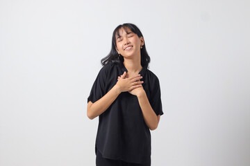 Portrait of attractive Asian woman in casual shirt placing hand on chest and feeling peaceful. Mental health day concept, expresses sympathy and love, smiles positively. Isolated on white background