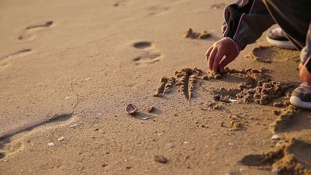 a child's hand writing his name on the beach
